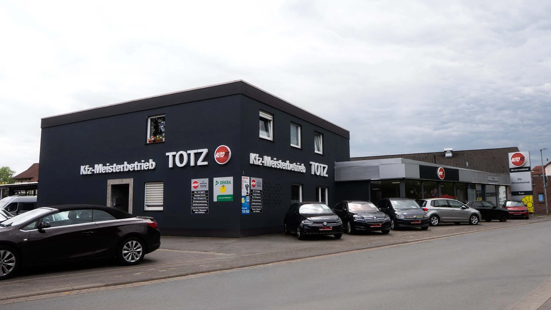 Anthrazitfarbenes Betriebsgebaeude von Autohaus Totz mit Fahrzeugen davor